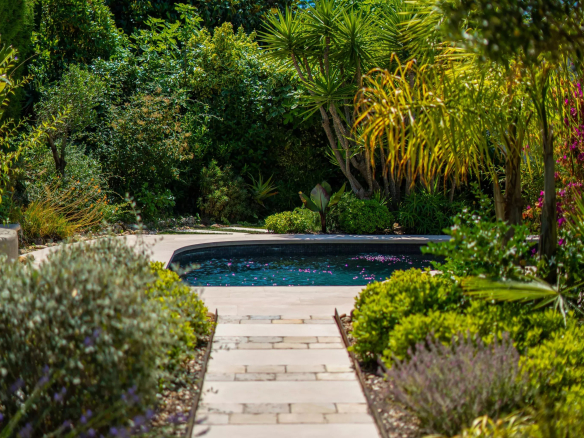 Path leading to a swimming pool surrounded by lush vegetation in a villa in Mougins.