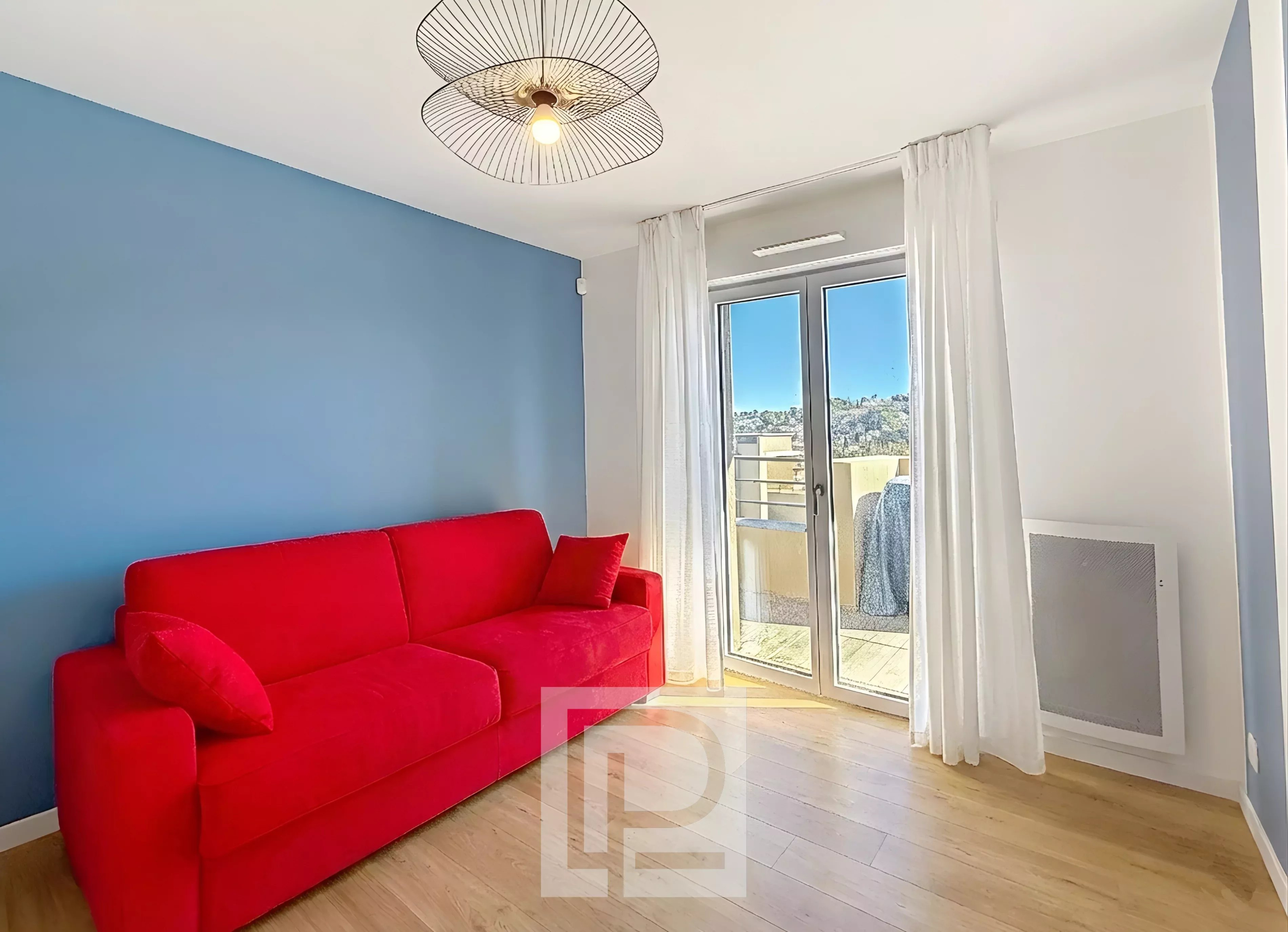 Salon d’appartement à Mougins Salon d'un appartement moderne avec canapé rouge et accès à un balcon, vue sur les collines.