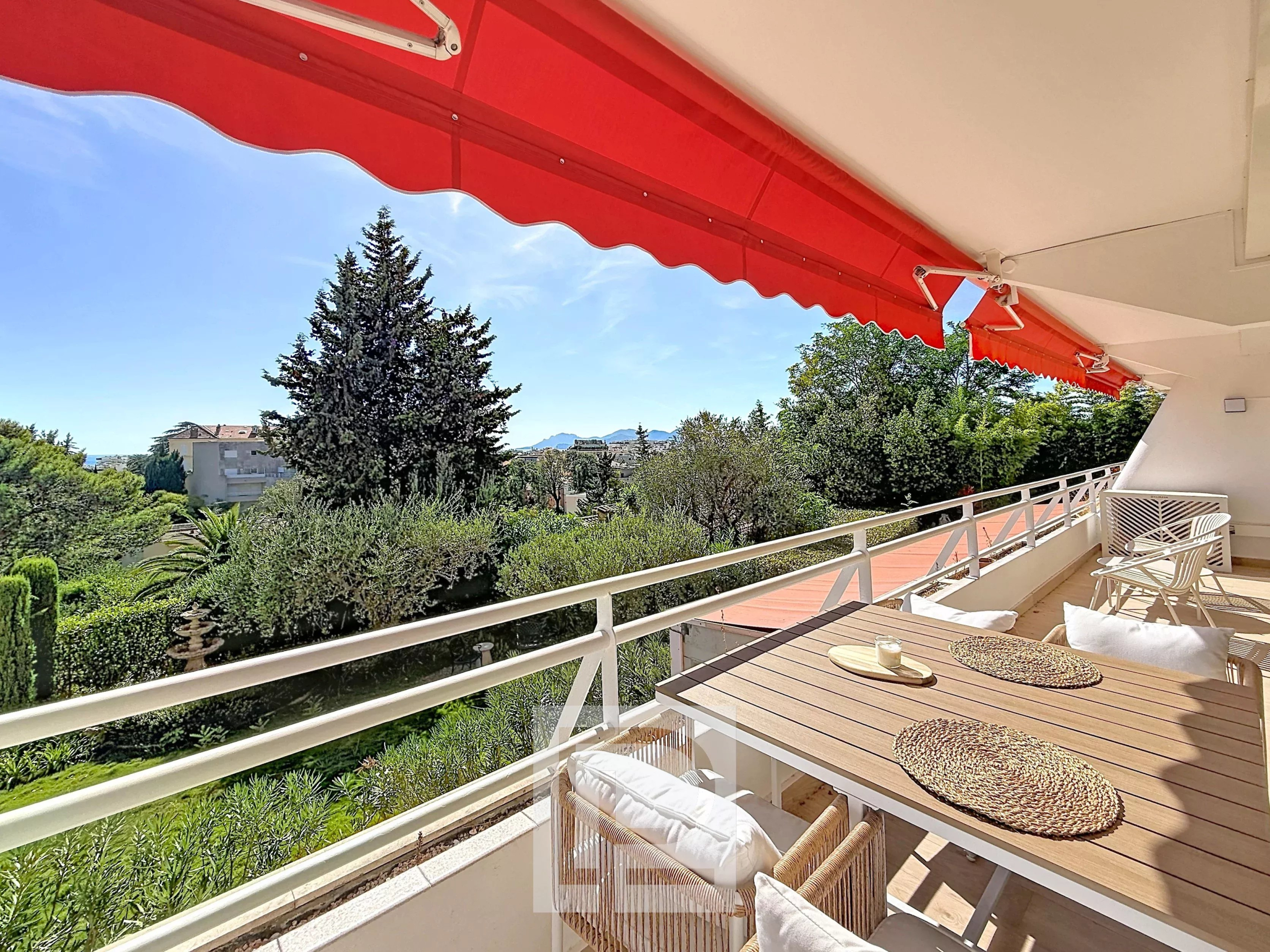 Balcon d’un appartement à Cannes Balcon d'un appartement rénové à Cannes avec vue sur la verdure et un ciel ensoleillé.