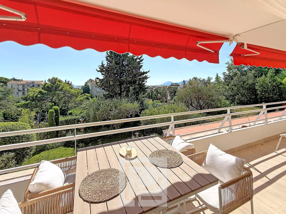 Terrasse d'un appartement rénové avec vue sur la verdure à Cannes, mobilier en bois et parasols rouges.