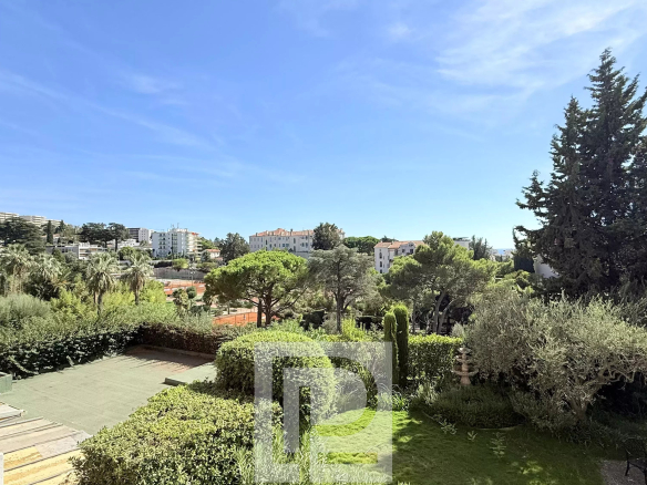 Vue dégagée sur un jardin et des bâtiments à Cannes depuis un appartement rénové.