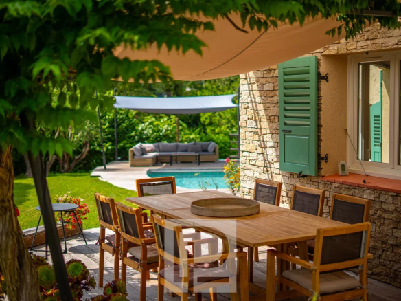 Terrasse en bois avec table à manger et piscine, entourée de verdure dans une villa provençale à Mougins.