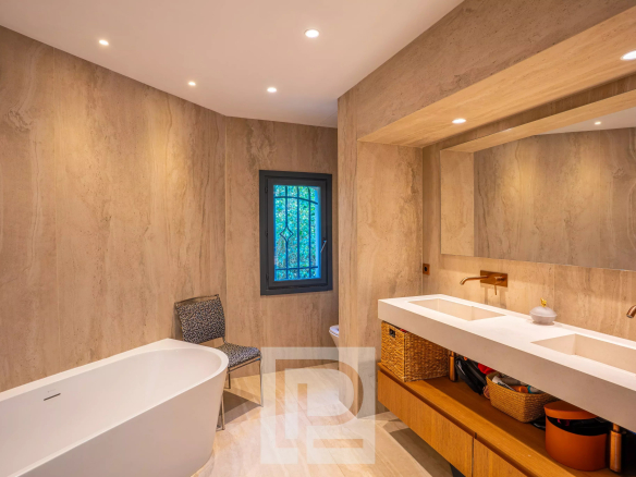 Salle de bain moderne avec baignoire et double vasque, murs en pierre beige.