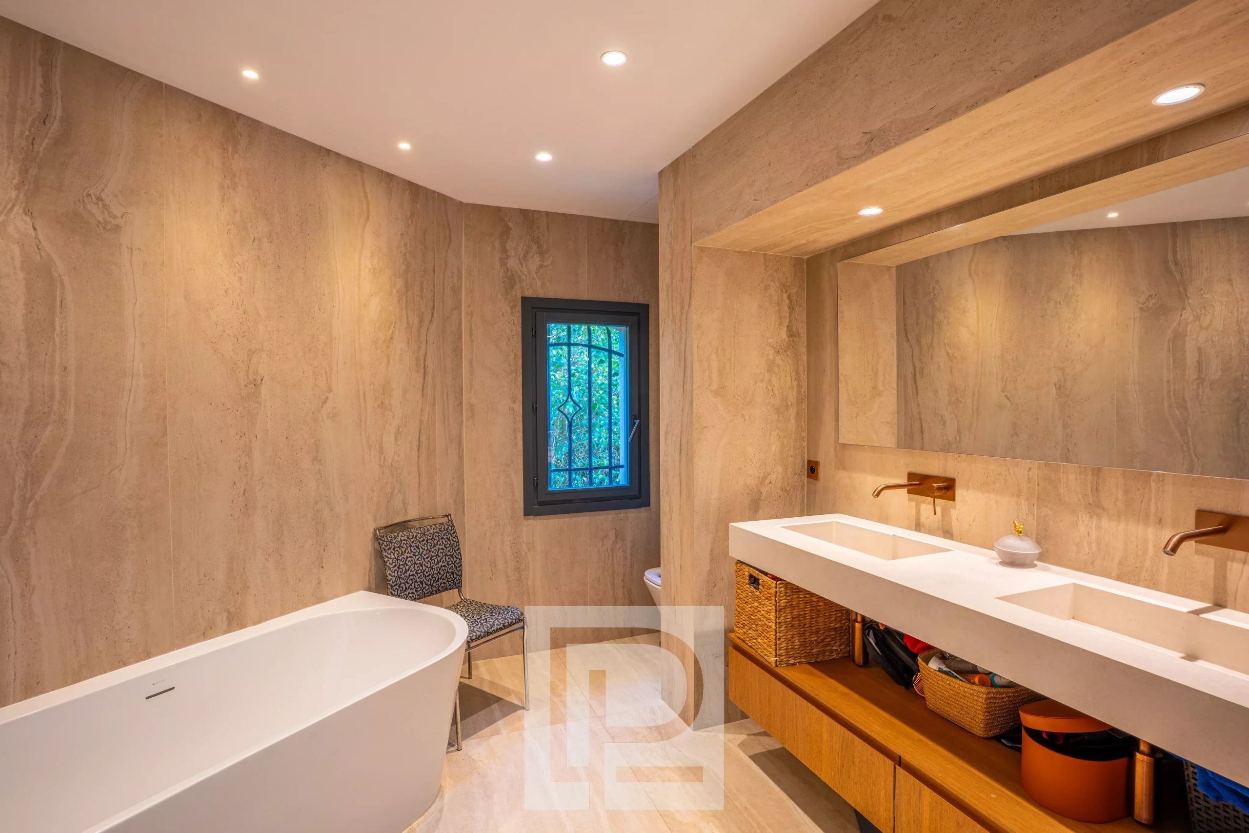 Salle de bain moderne avec baignoire et double vasque, murs en pierre beige.