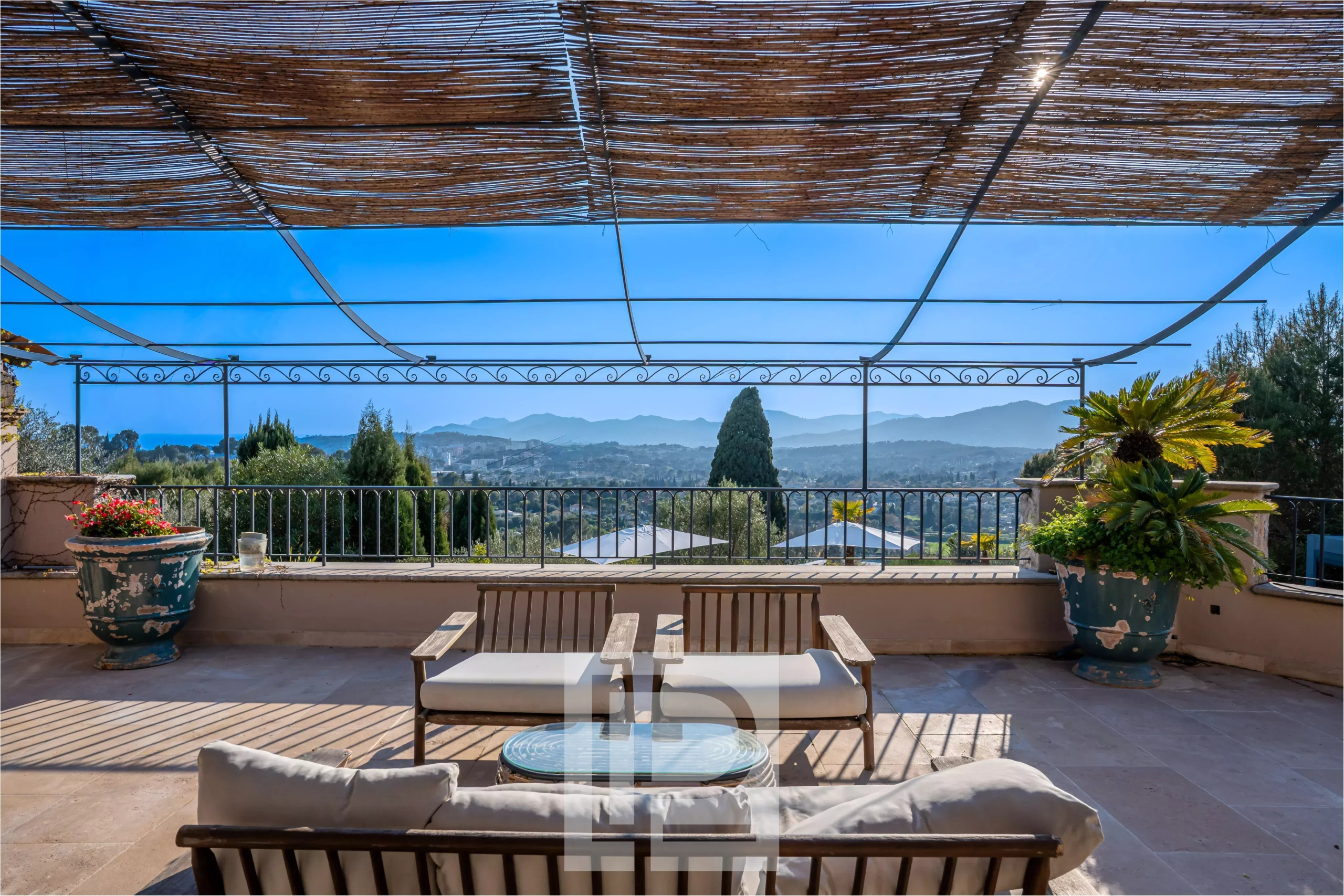 Terrasse avec vue panoramique sur les collines et la mer, mobilier de jardin en bois.