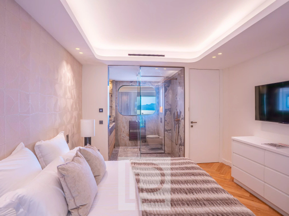 Chambre lumineuse d'un appartement moderne avec salle de bain vitrée et vue sur la mer.