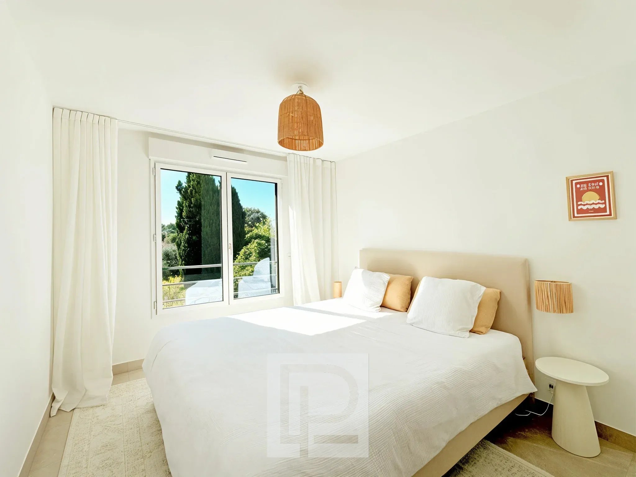 Chambre d’appartement à Mougins Chambre lumineuse avec lit double et fenêtre donnant sur un espace vert.