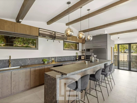 Cuisine moderne et spacieuse d'une villa en pierre rénovée à Valbonne, avec îlot central et vue dégagée.