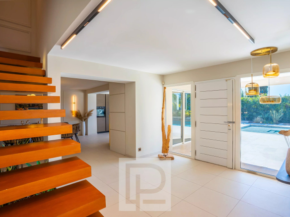 Intérieur d'une villa contemporaine avec escalier en bois et grandes fenêtres donnant sur l'extérieur.