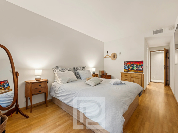 Chambre d'un appartement rénové avec lit double, mobilier en bois et miroir, dans une résidence avec piscine.
