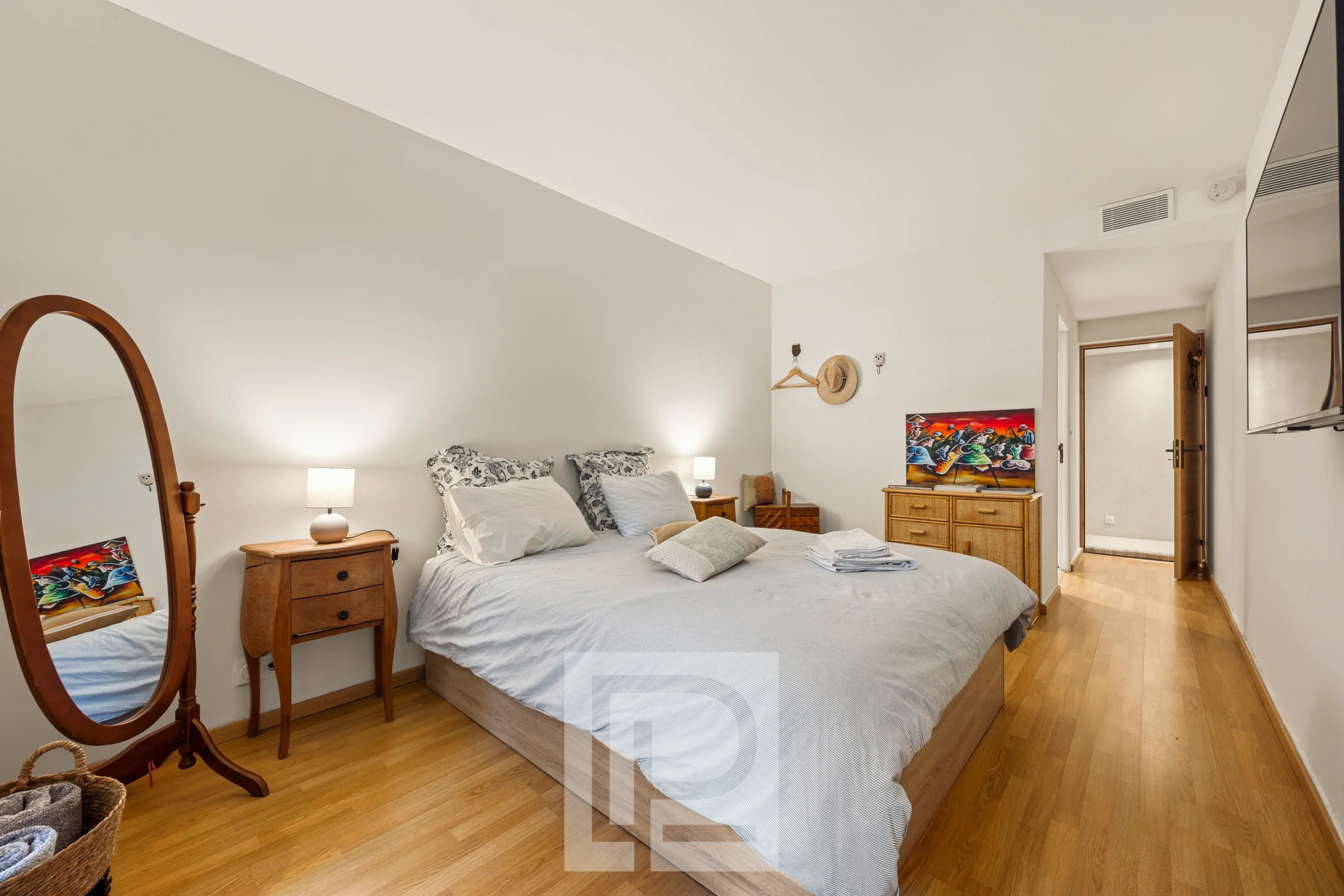Chambre élégante d’un appartement rénové Chambre d'un appartement rénové avec lit double, mobilier en bois et miroir, dans une résidence avec piscine.