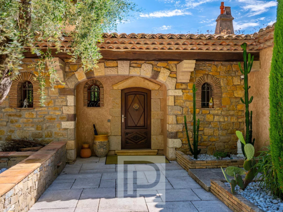 Entrance to a stone property with plants and a flagstone path, located in Mouans-Sartoux.