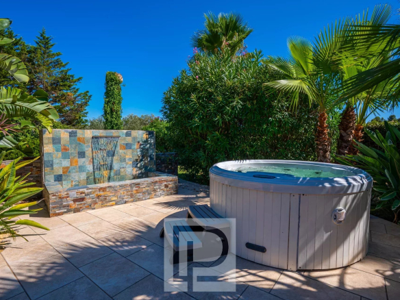 Outdoor area of ​​a property with jacuzzi and water wall, surrounded by lush vegetation.