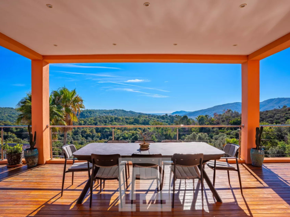 Terrasse avec vue panoramique sur la nature et la mer, entourée de verdure.
