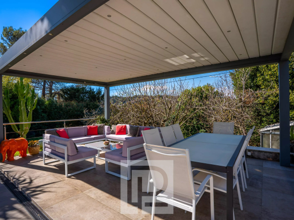 Terrasse d'une villa californienne avec salon extérieur et table à manger, entourée de verdure.