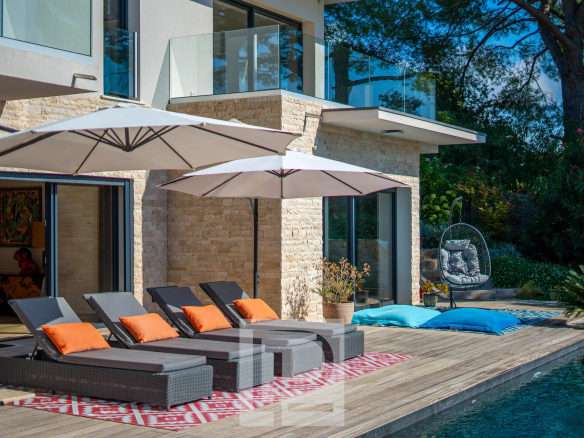 Villa contemporaine avec piscine, chaises longues et parasols, entourée de verdure à Mougins.