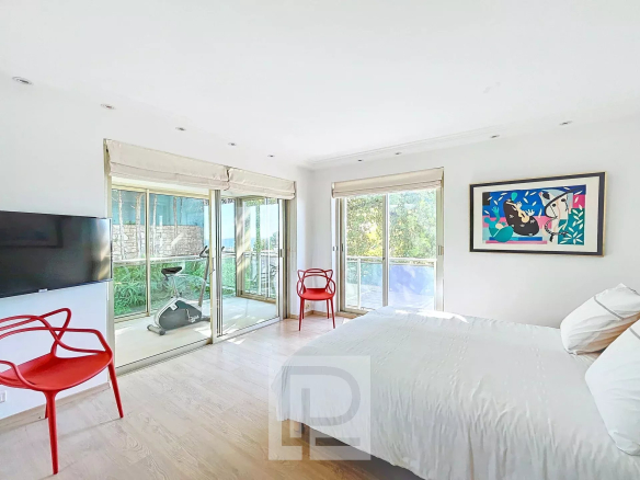 Chambre lumineuse avec accès à un balcon, équipée d'un téléviseur et de chaises rouges.