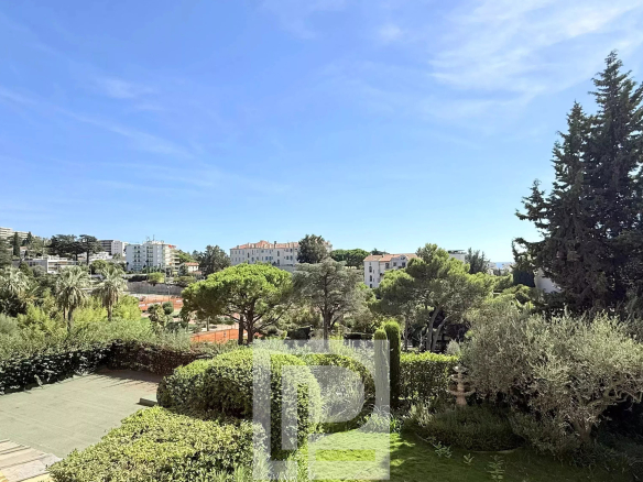 Vue dégagée sur un jardin et des bâtiments à Cannes depuis un appartement rénové.