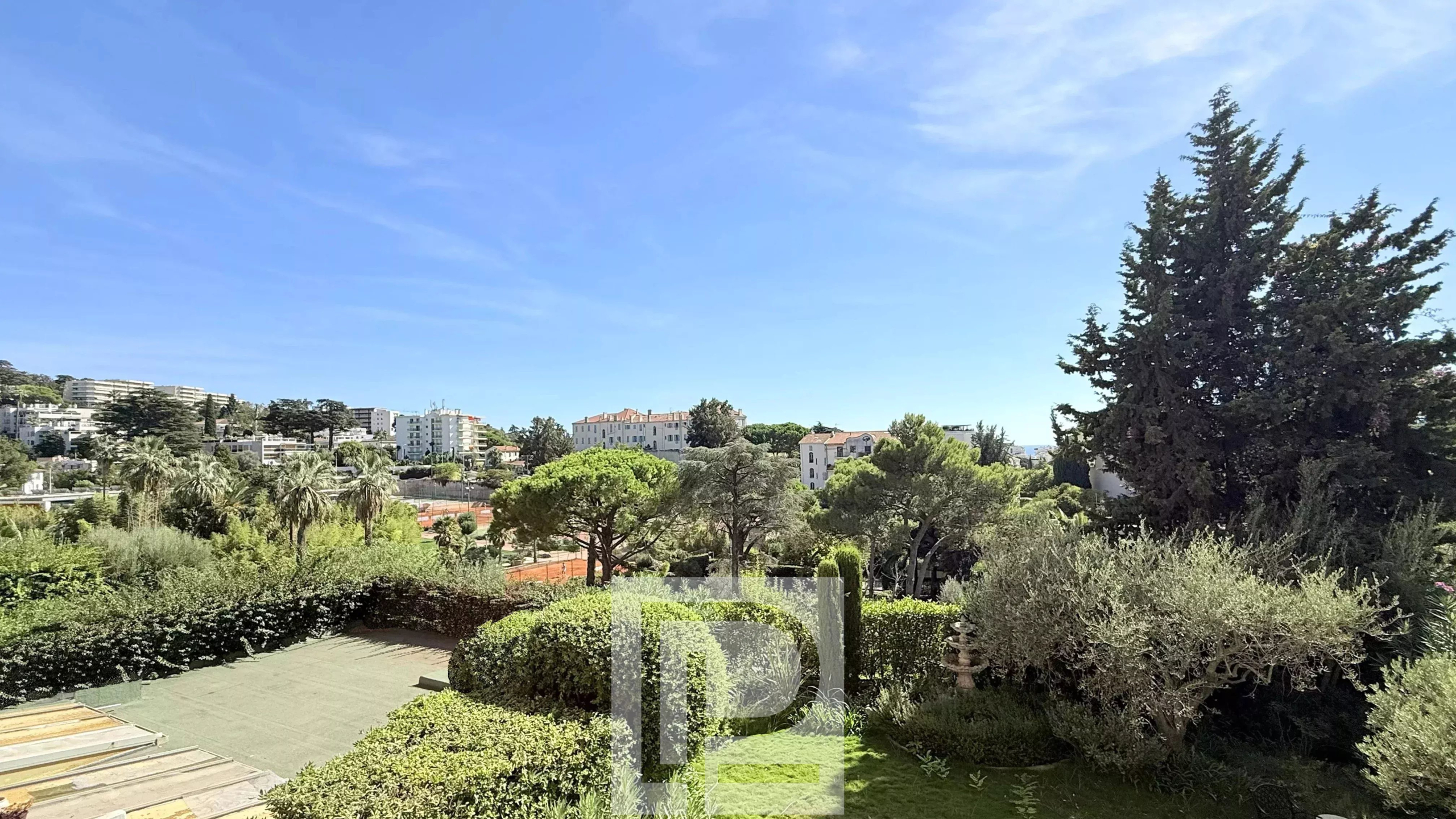 Vue dégagée sur un jardin et des bâtiments à Cannes depuis un appartement rénové.