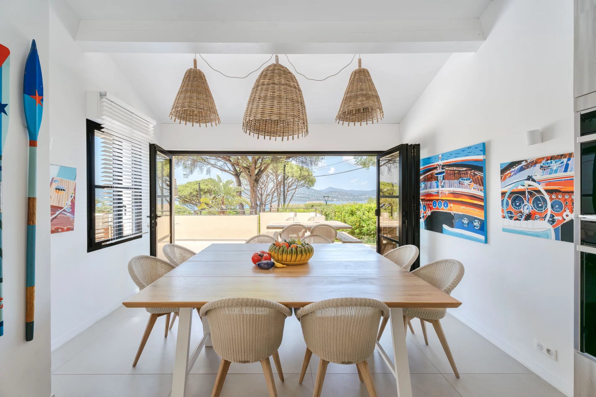 Salle à manger avec vue mer Salle à manger lumineuse avec vue sur la mer, décorée de tableaux, dans une villa à Gassin.