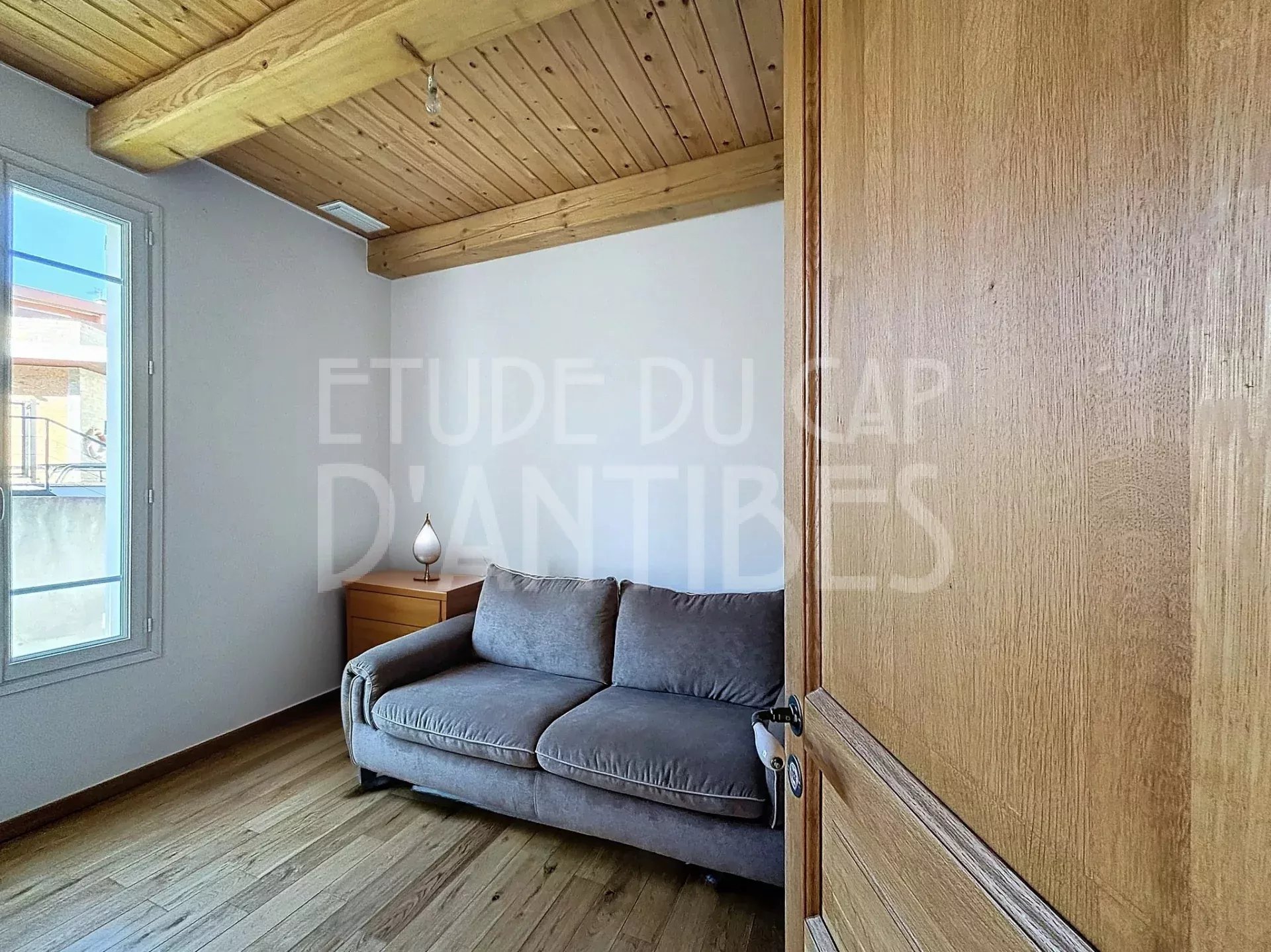 Cozy living room corner with a gray sofa, wooden side table and lamp under exposed wood beams.