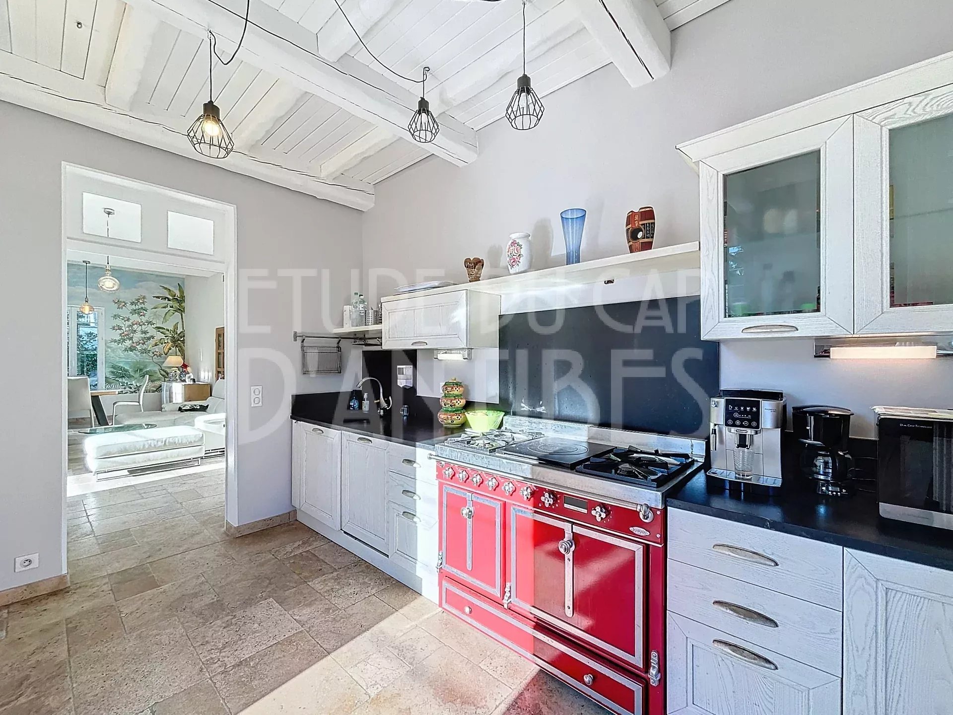 Bright kitchen with white cabinets, black countertops, and a striking red vintage stove as the focal point under beamed ceilings and pendant lights.