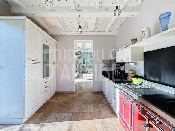 Bright kitchen with white cabinets and a red vintage stove, open doorway to a sunny dining area.