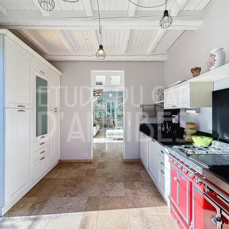 Bright kitchen with white cabinets and a red vintage stove, open doorway to a sunny dining area.