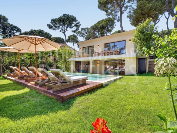Villa moderne avec piscine et chaises longues dans un jardin arboré à Antibes.