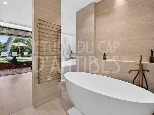 Salle de bain moderne avec baignoire, vue sur le jardin et la piscine.