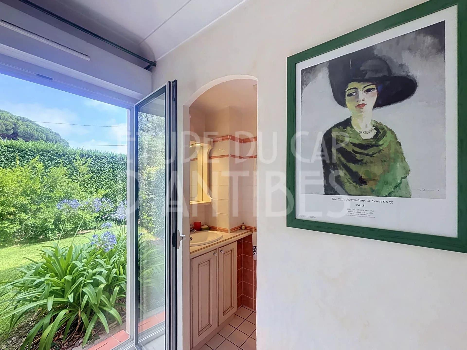 Intérieur d'un appartement avec une porte ouverte sur un jardin, peinture au mur.