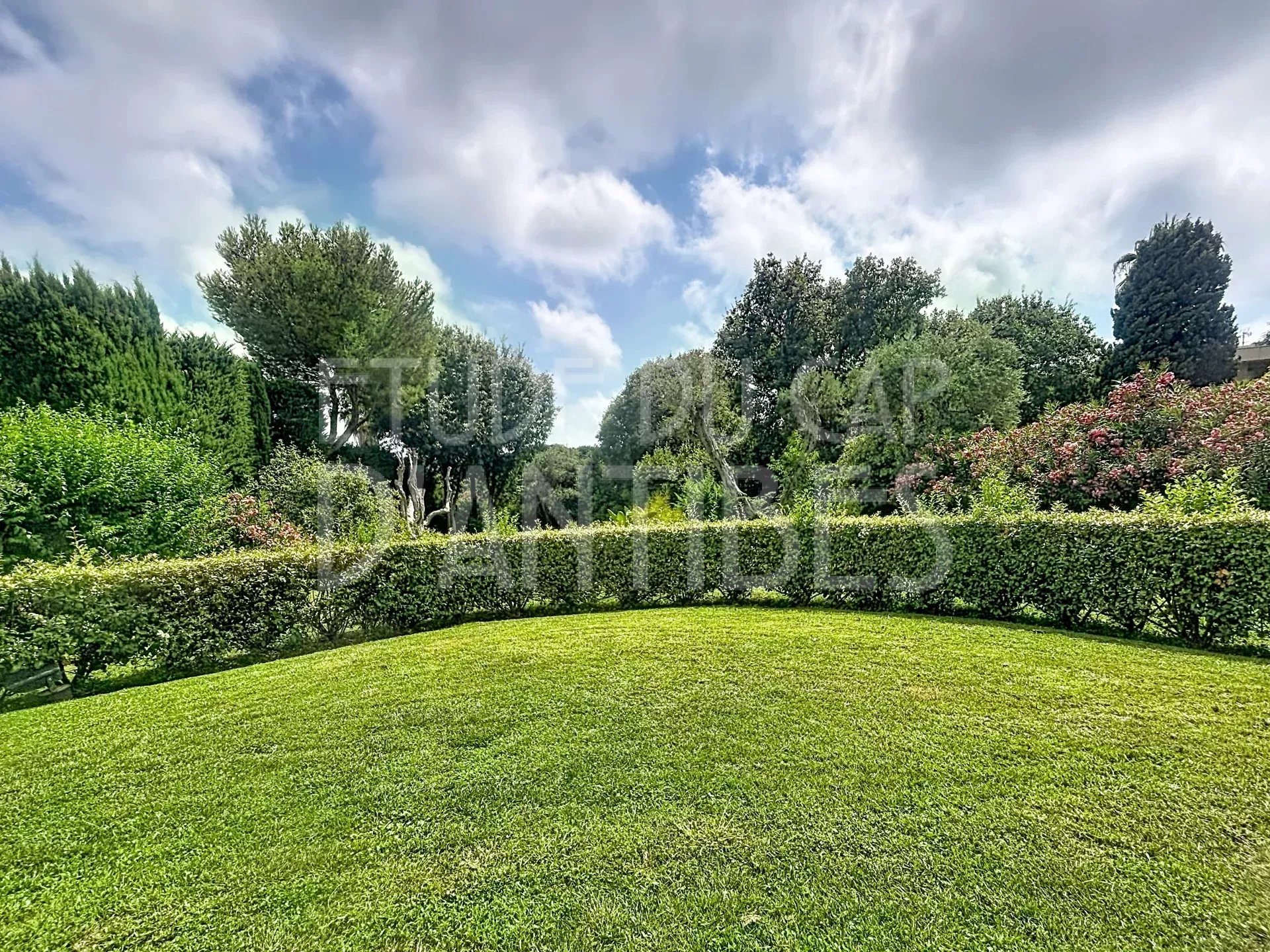 Jardin privatif d'un appartement dans une résidence avec piscine à Antibes, entouré de verdure.