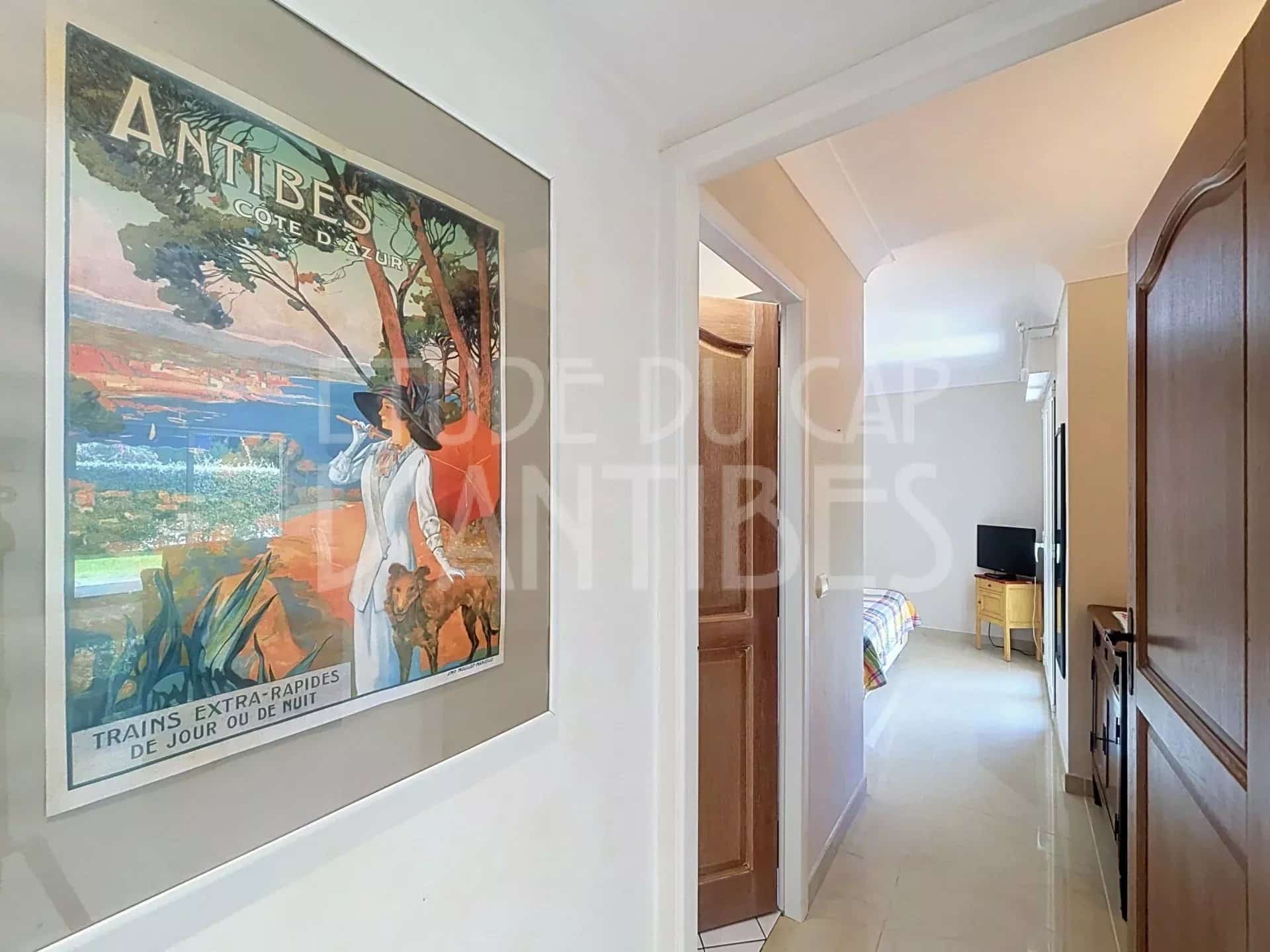 Intérieur d'un appartement à Antibes avec un couloir menant à un salon et une décoration murale.