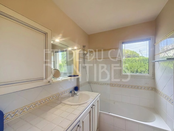 Salle de bain lumineuse avec baignoire et lavabo, fenêtre donnant sur l'extérieur.
