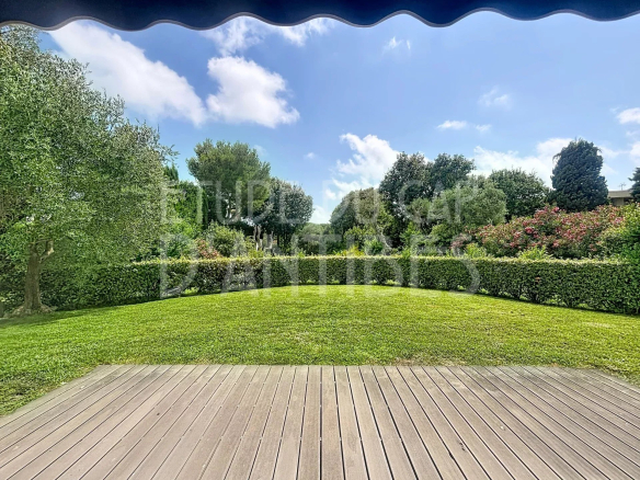 Vue du jardin privatif d'un appartement à Antibes, avec pelouse et haies verdoyantes sous un ciel bleu.