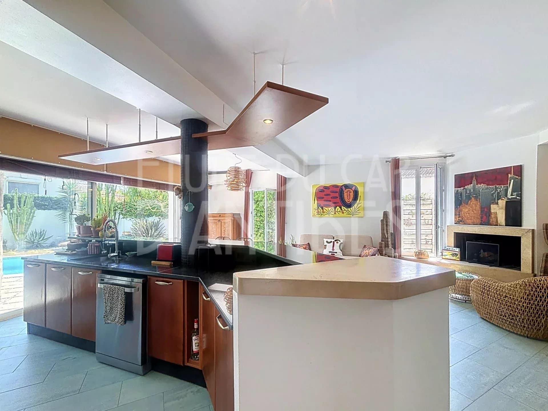 Intérieur d'une villa méditerranéenne avec cuisine ouverte et salon lumineux, piscine visible à l'extérieur.