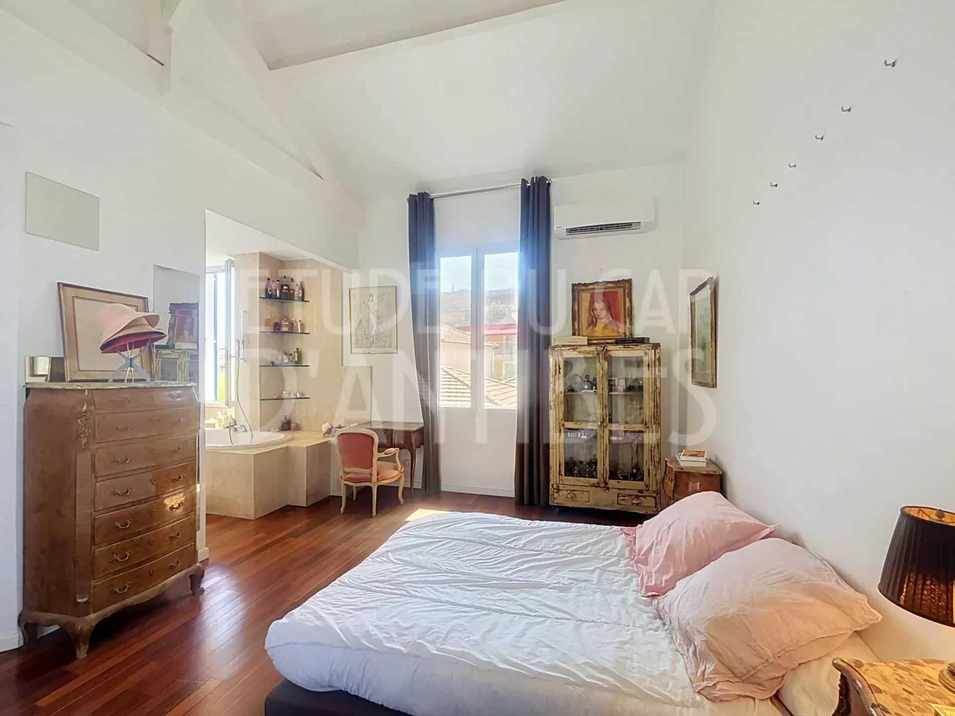 Chambre d'une villa méditerranéenne à Antibes avec lit, meubles en bois et lumière naturelle.