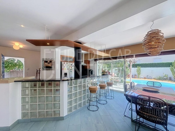 Intérieur d'une villa méditerranéenne avec cuisine ouverte et bar, vue sur la piscine.