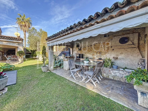 Terrasse avec coin repas et barbecue dans une villa à Cap d'Antibes, jardin verdoyant en arrière-plan.