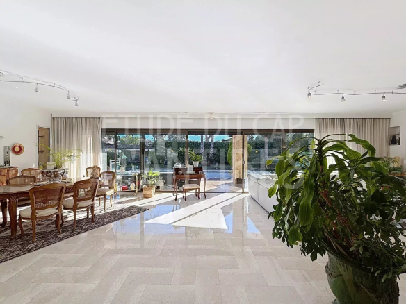 Intérieur lumineux d'une villa avec salon et salle à manger, grandes baies vitrées donnant sur la piscine.