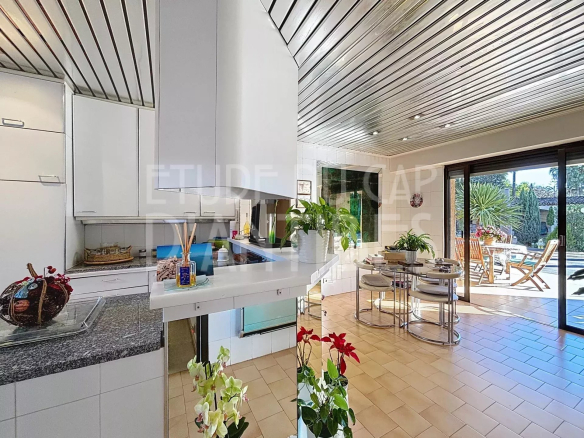 Intérieur d'une villa lumineuse avec cuisine ouverte et salle à manger, vue sur la terrasse et la piscine.