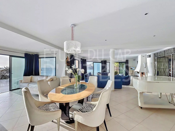 Intérieur d'une villa moderne avec salle à manger et salon lumineux, vue sur la mer.
