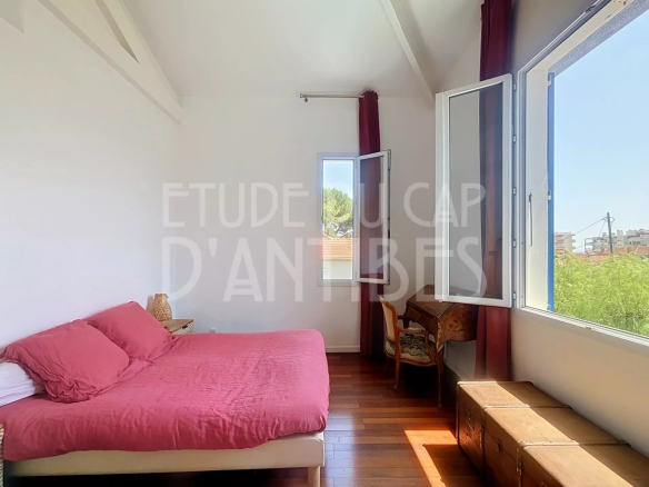 Chambre d'une villa méditerranéenne à Antibes avec lit et fenêtres ouvertes.