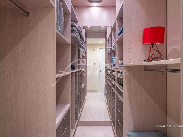 Walk-in closet with light wood shelves on both sides, folded towels, and a red desk lamp on the right side.