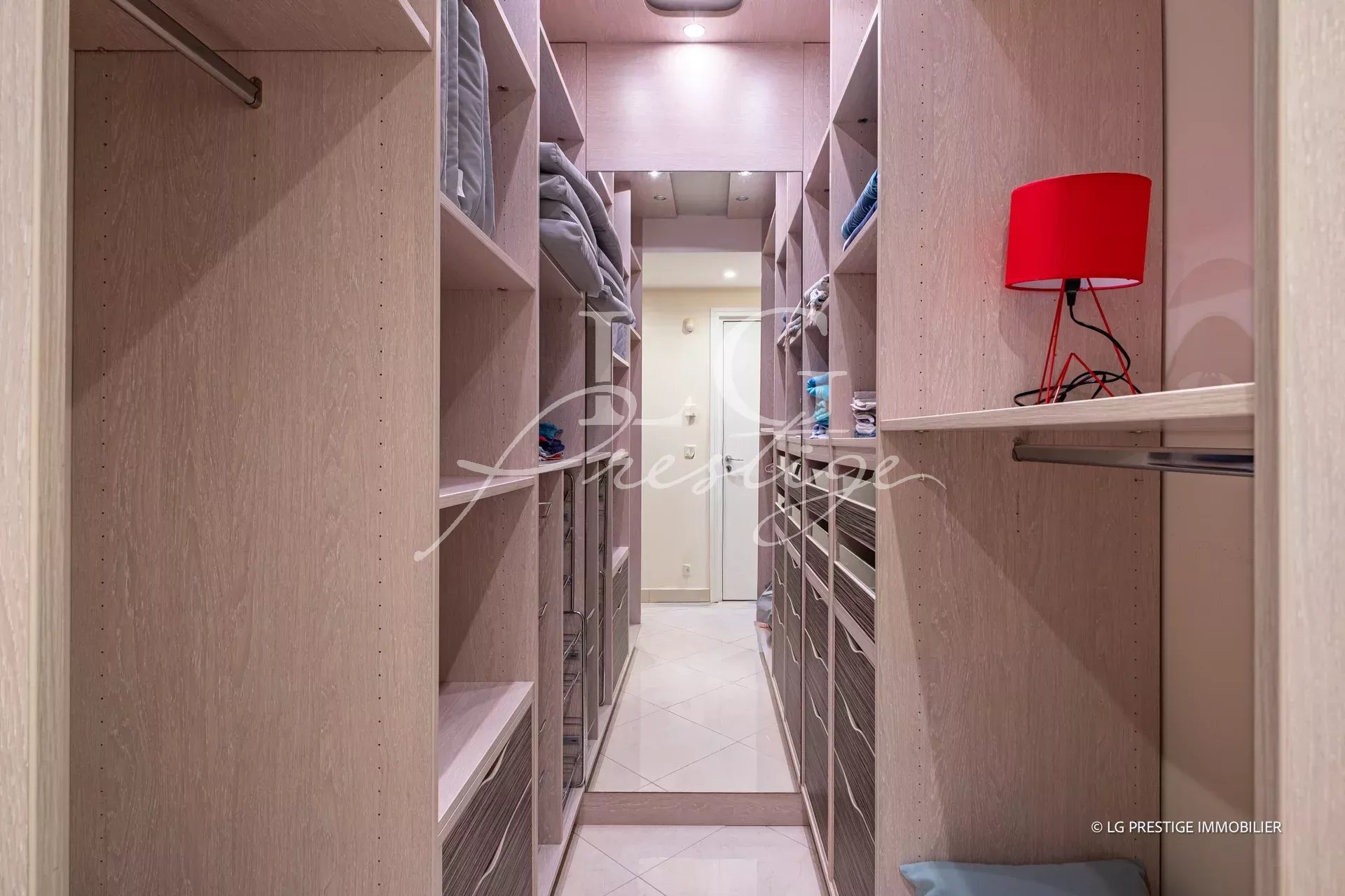 Walk-in closet with light wood shelves on both sides, folded towels, and a red desk lamp on the right side.