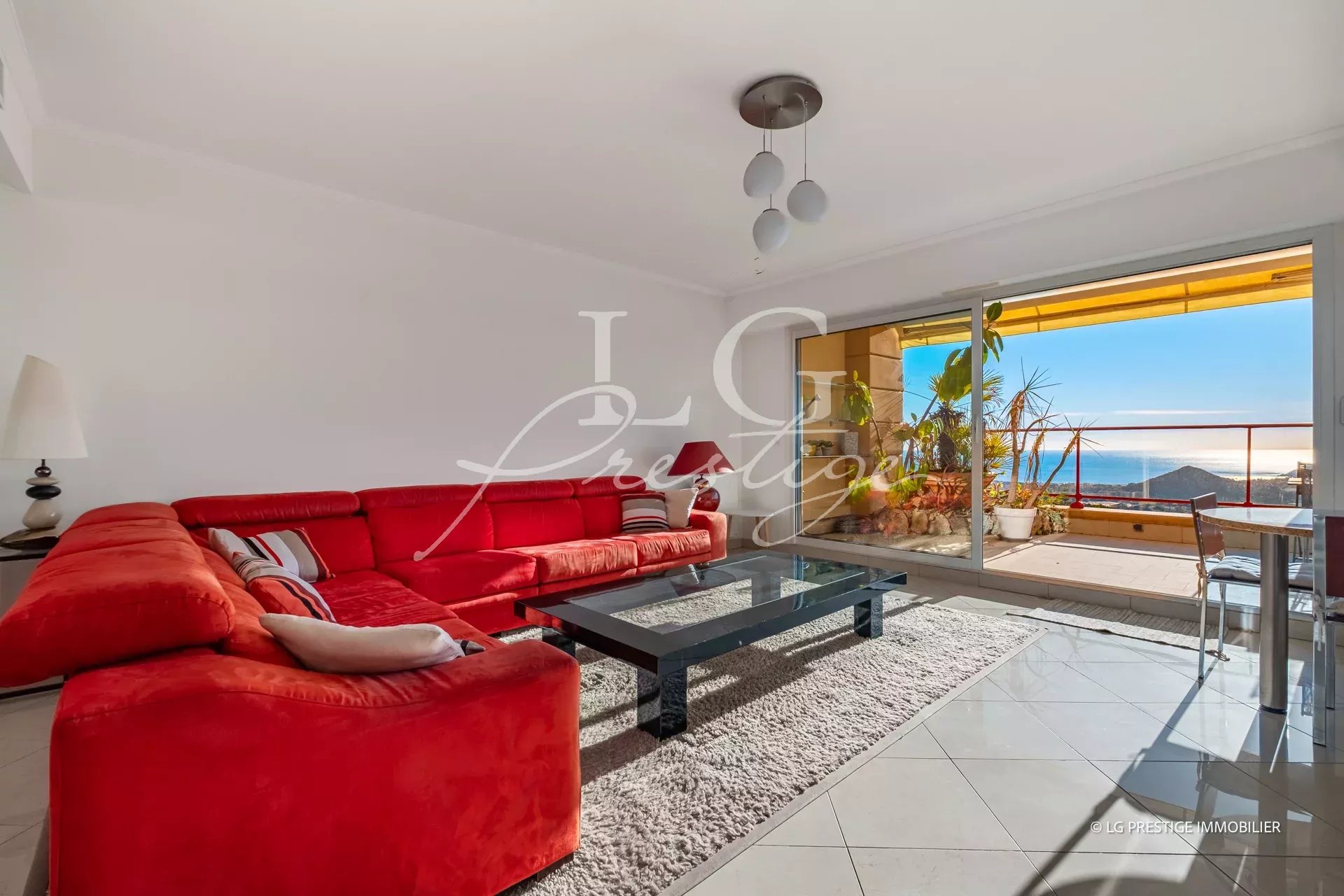Bright living room with a red sectional sofa, glass coffee table, and balcony doors to an ocean view.
