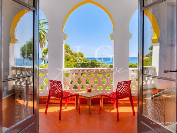 View from a balcony with two red chairs, overlooking a park and the sea in Cannes.