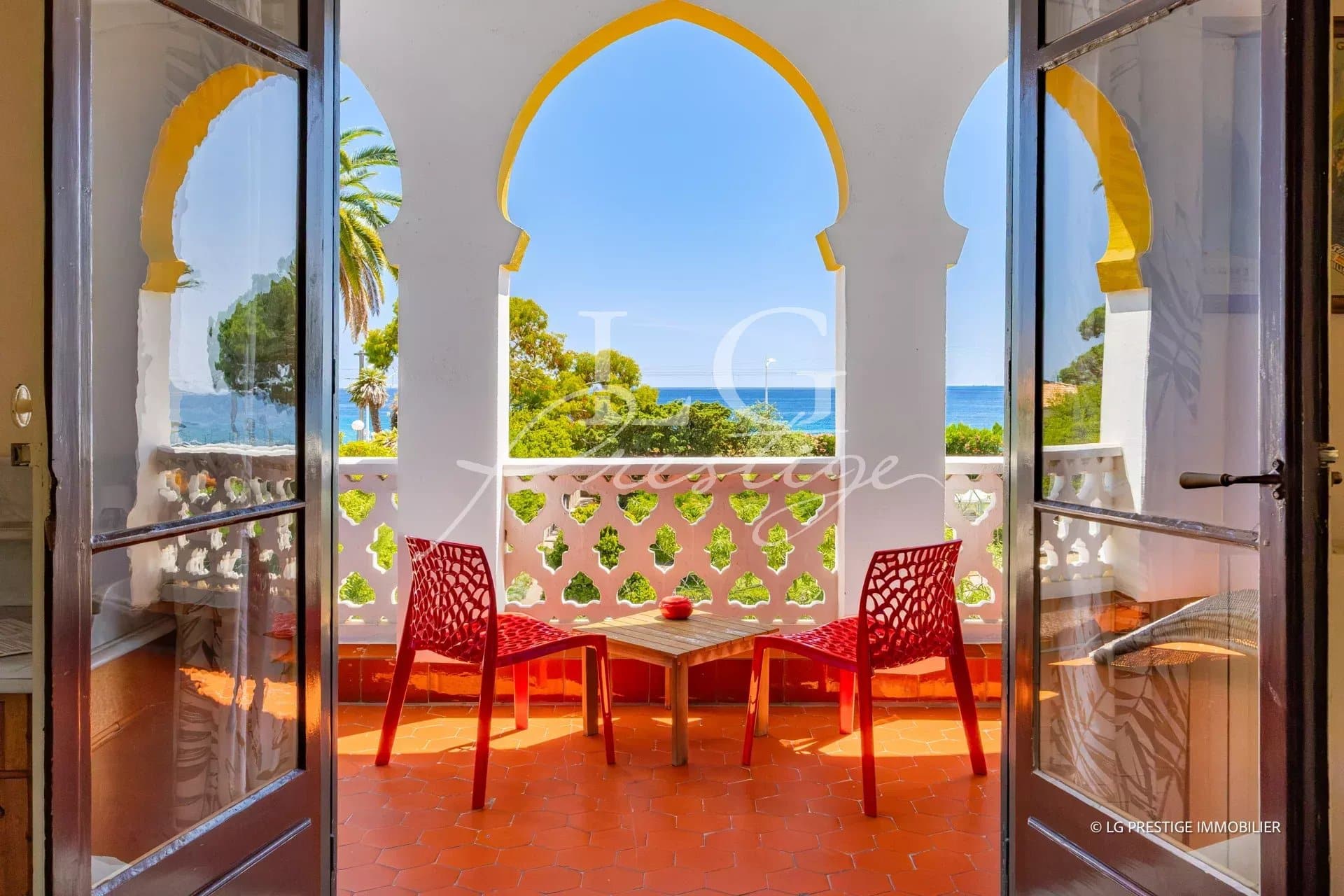 View from a balcony with two red chairs, overlooking a park and the sea in Cannes.