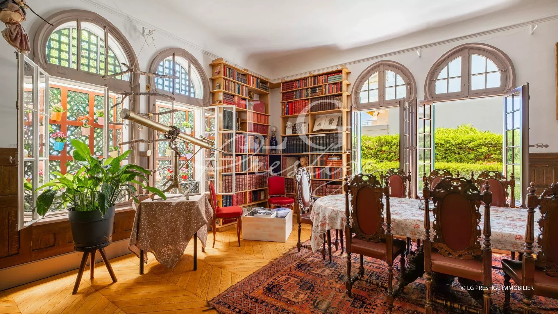 Interior of an elegant dining room with arched windows and bookshelves filled with books.