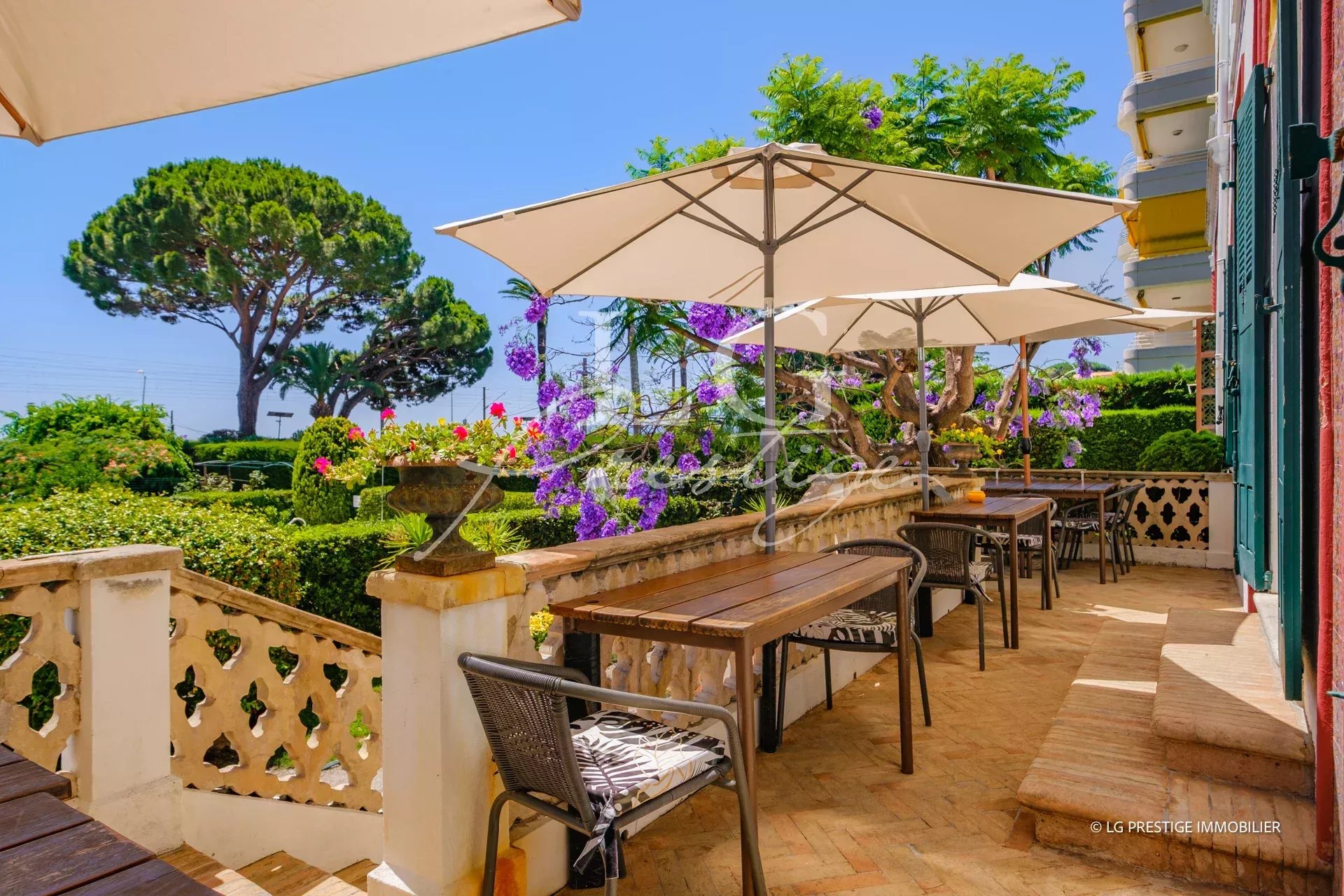 Terrace with wooden tables and parasols, surrounded by greenery and flowers in Cannes.